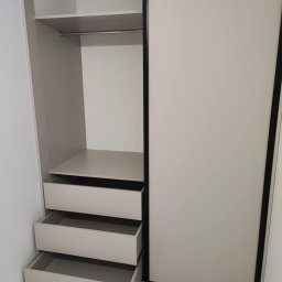 Mateusz Otwinowski Build & Design - Wnętrze szafy wnękowej z przesuwnymi drzwiami, widoczne półki, drążek na ubrania i wysuwane szuflady. Jasna kolorystyka, minimalistyczny design.