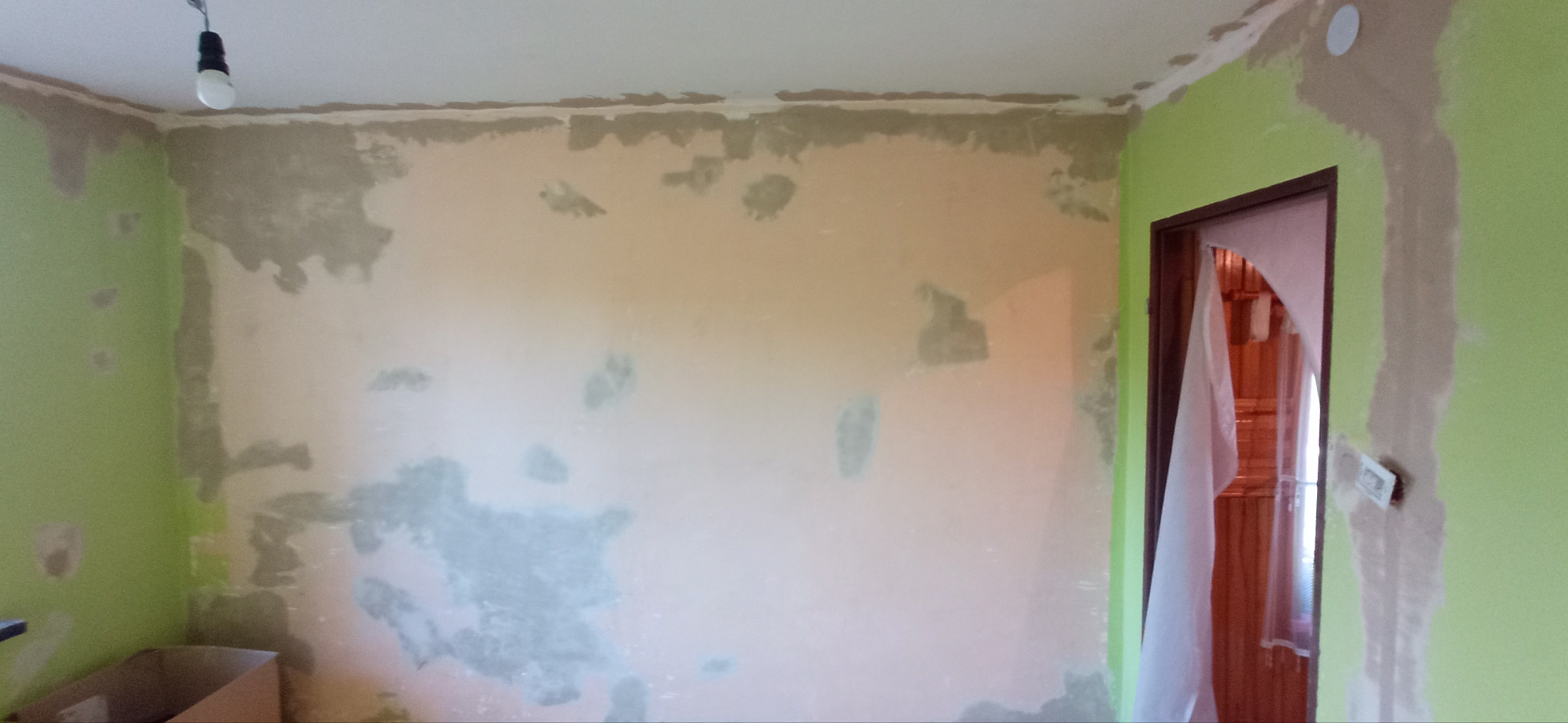 Pokój w trakcie przygotowywania ścian do malowania: częściowo zagruntowane ściany w odcieniach zieleni i beżu, widoczne ślady po szpachlowaniu, niezabezpieczone przewody elektryczne, drzwi...