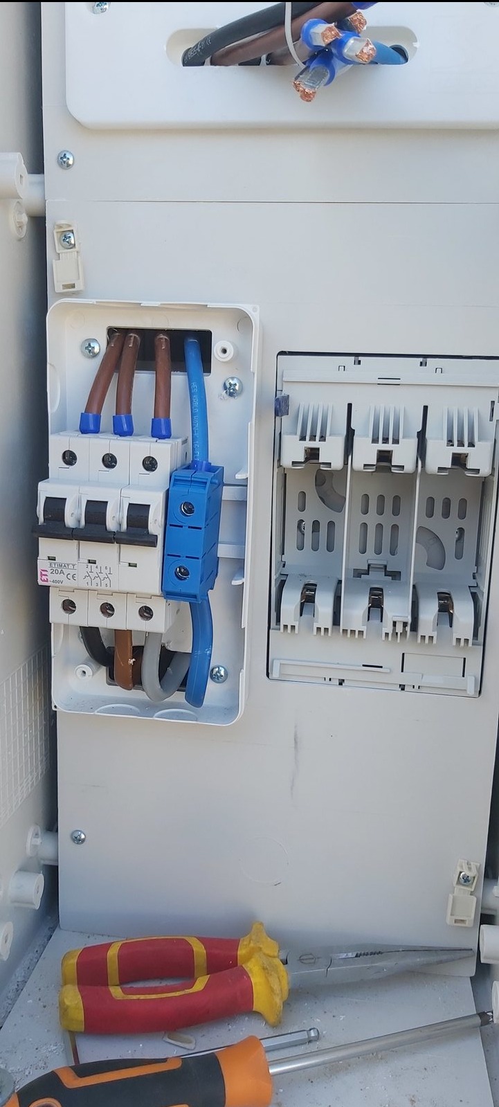 Rozdzielnica elektryczna w trakcie montażu z widocznymi przewodami, bezpiecznikami i narzędziami, ukazująca etap prac instalacyjnych.