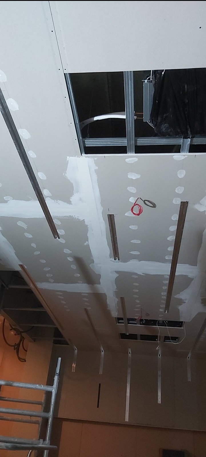 Sufit podwieszany z widoczną konstrukcją metalową i przewodami elektrycznymi w trakcie montażu, oświetlenie w tle.