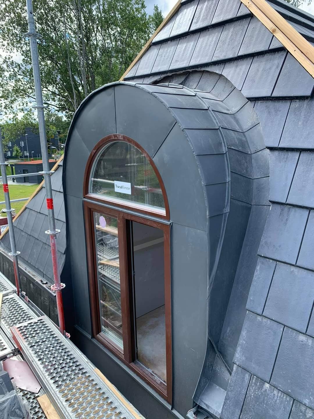 Dach z łupka z owalnym oknem dachowym i metalową obróbką, widok z rusztowania.