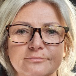 VAI - STUDIO DOROTA SUROWIŃSKA - Portret kobiety z siwymi włosami i okularami w rogowej oprawce, patrzącej wprost w obiektyw, z widocznym znamieniem na policzku.