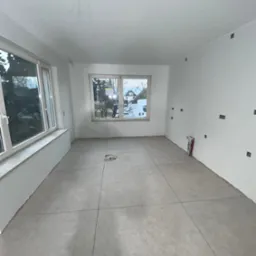 Wnętrze pokoju po gładziowaniu i malowaniu na biało, widoczne przygotowane punkty elektryczne, okna z widokiem na zewnątrz i przygotowana podłoga pod panele.