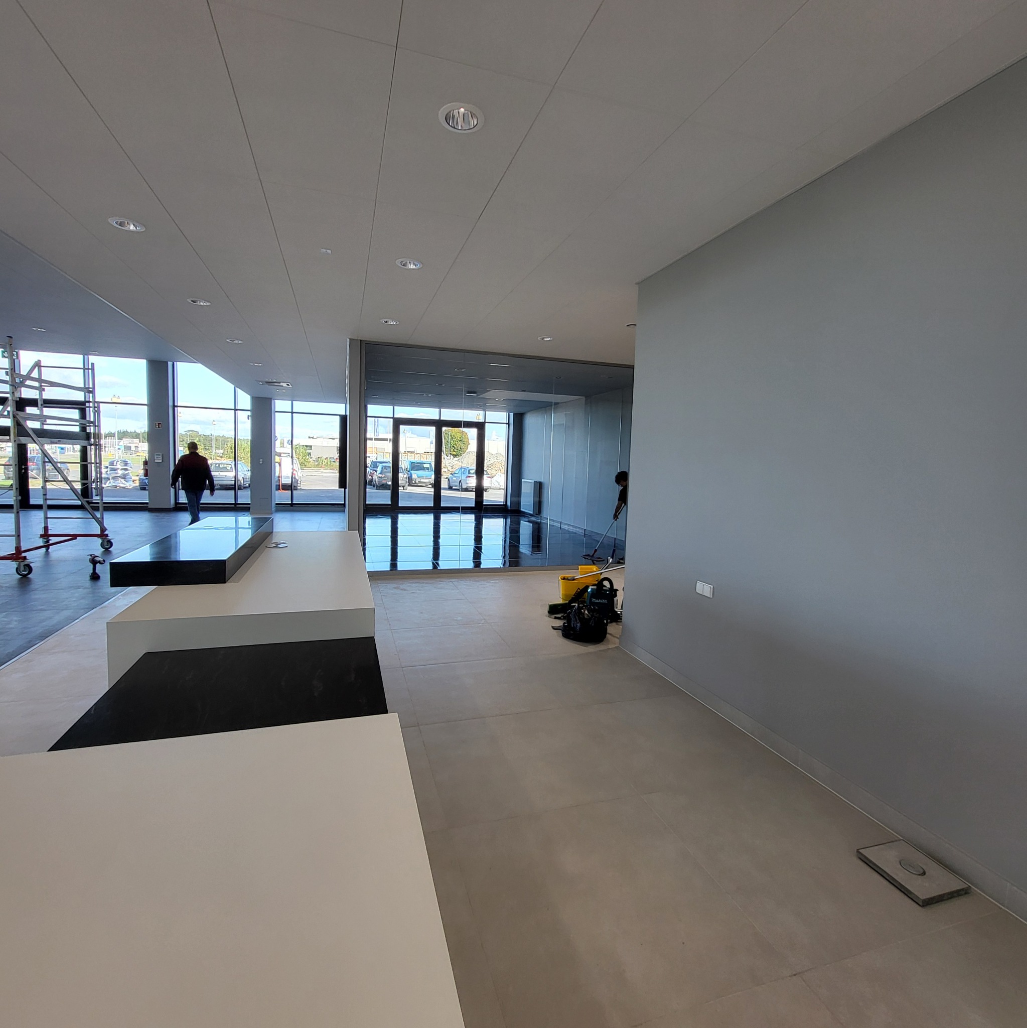 Wnętrze nowoczesnego biura z pracownikiem myjącym podłogę, widoczne duże okna, minimalistyczne meble i sprzęt do utrzymania czystości.