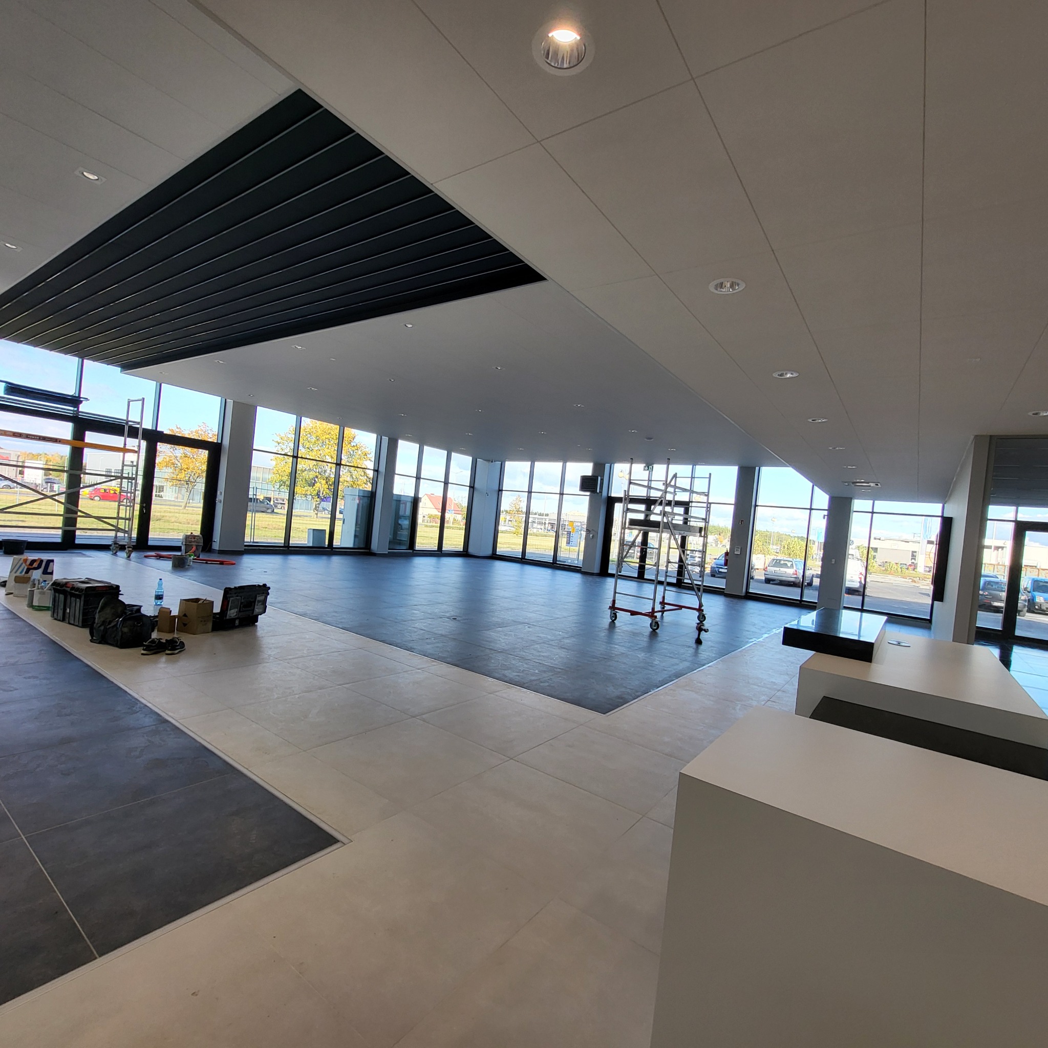 Przestronne wnętrze biurowe z dużymi oknami, na podłodze widoczne ślady po remoncie, w tle rusztowanie i narzędzia.