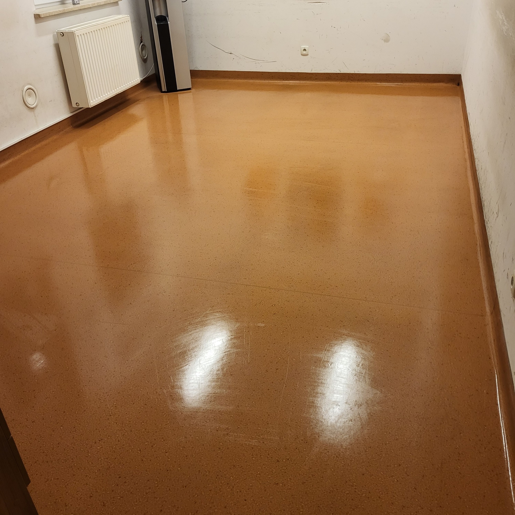 Błyszcząca, świeżo umyta podłoga z terakoty w pustym pomieszczeniu biurowym z grzejnikiem i dystrybutorem wody przy ścianie.