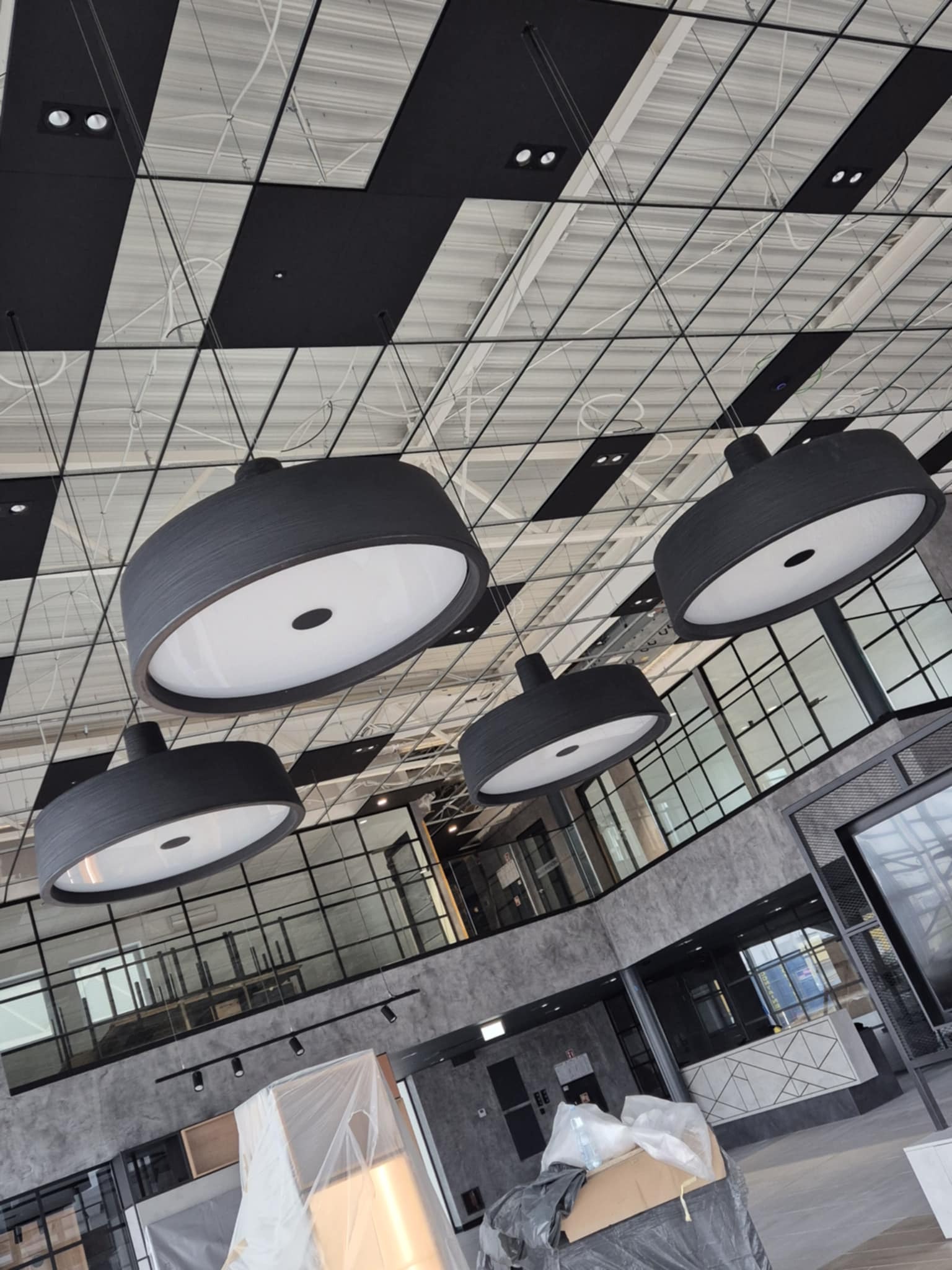 Wnętrze biura w trakcie sprzątania po remoncie, widoczne lampy sufitowe, okna i meble zabezpieczone folią.