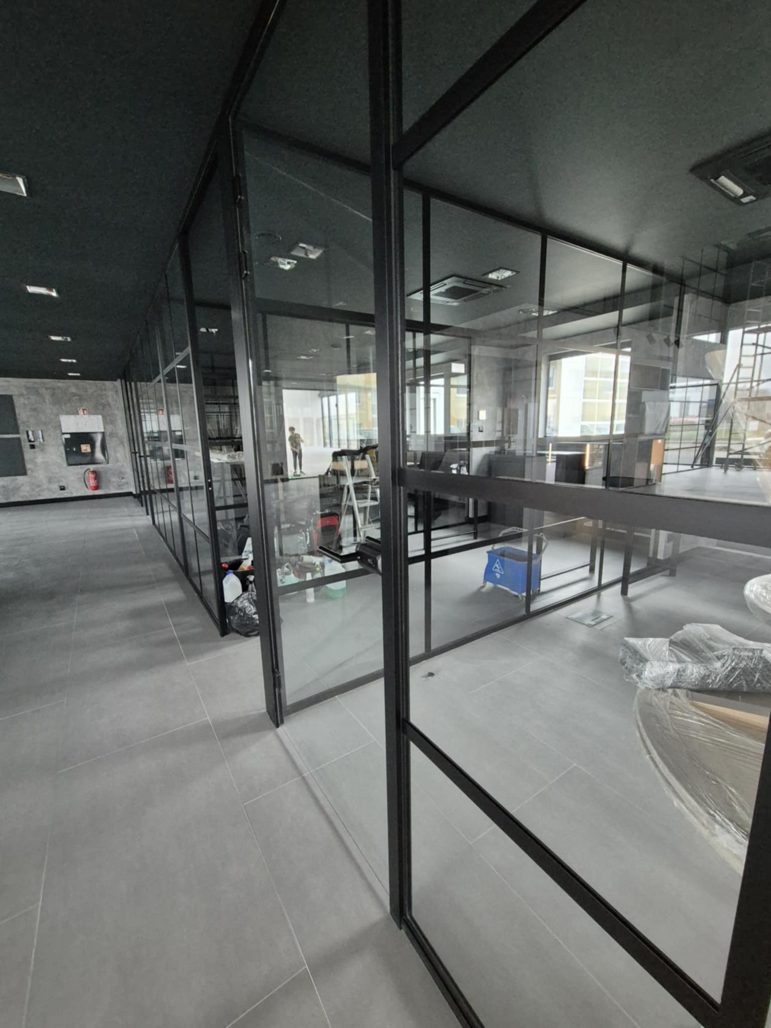 Nowoczesne biuro z przeszklonymi ścianami działowymi, widoczne ślady po remoncie: drabina, wiadro, folia ochronna na meblach.