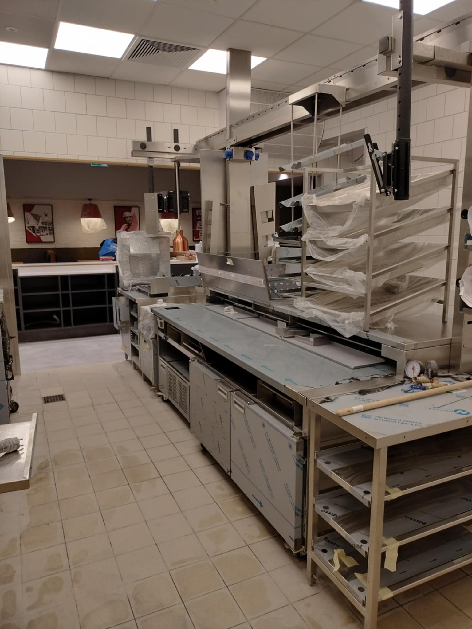 Wnętrze kuchni przemysłowej po remoncie, widoczne nowe, nierozpakowane urządzenia ze stali nierdzewnej, podłoga z zabrudzeniami po pracach budowlanych.