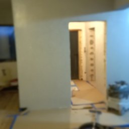 Firma remontowo-budowlane Łukasz Szymczak - Przygotowania do remontu mieszkania: zabezpieczona podłoga drewniana taśmą malarską, widoczny odkurzacz przemysłowy i sprzęt malarski w tle, ściany częściowo pokryte gładzią.