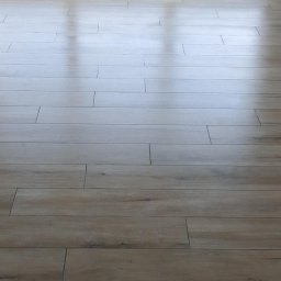 Firma remontowo-budowlane Łukasz Szymczak - Ułożona podłoga z paneli imitujących drewno w jasnym odcieniu, widoczne fugi i odbicie światła słonecznego na powierzchni.