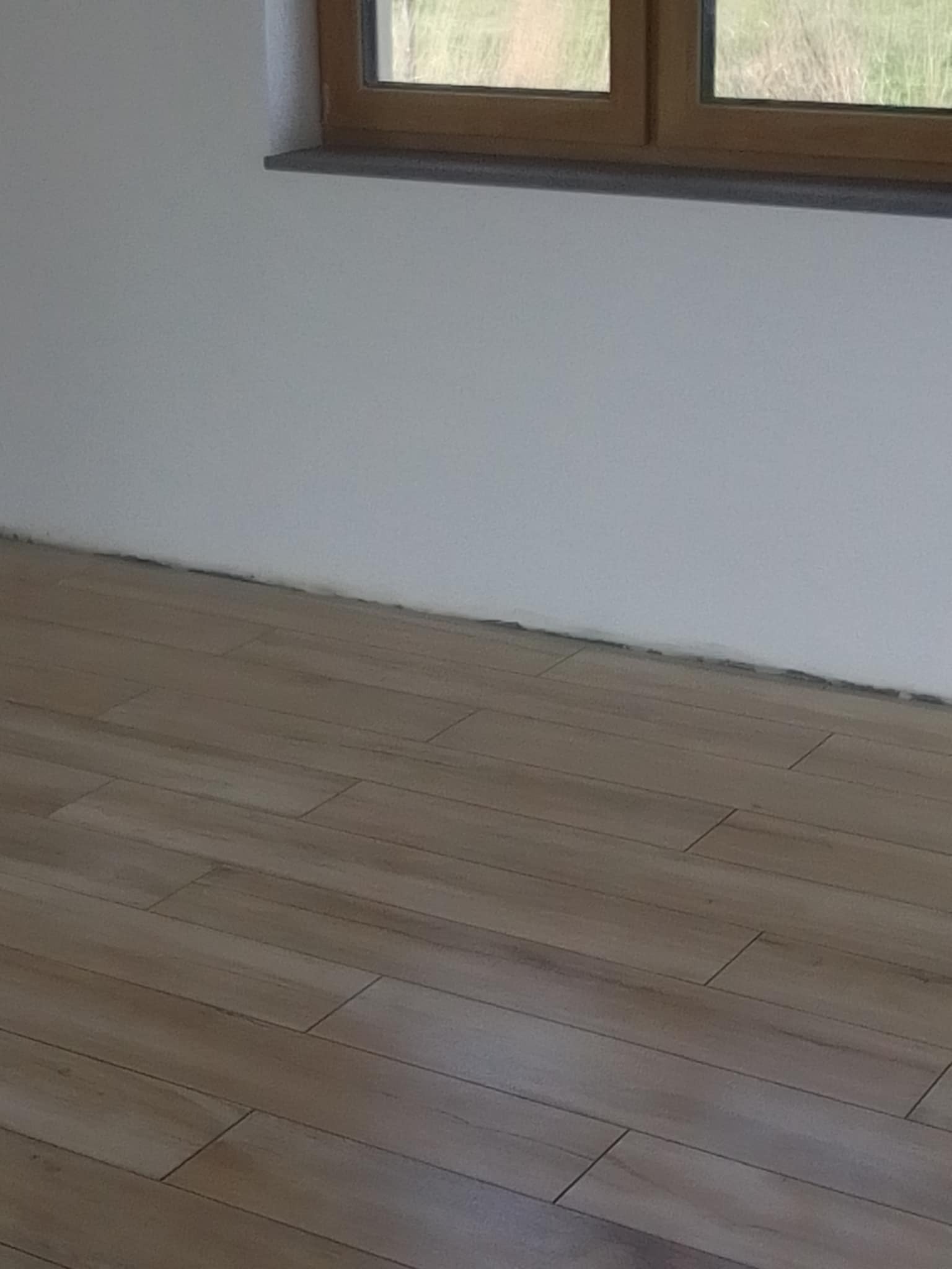 Ułożone panele podłogowe imitujące drewno w jasnym, nowym pomieszczeniu z białymi ścianami i oknem w drewnianej ramie.