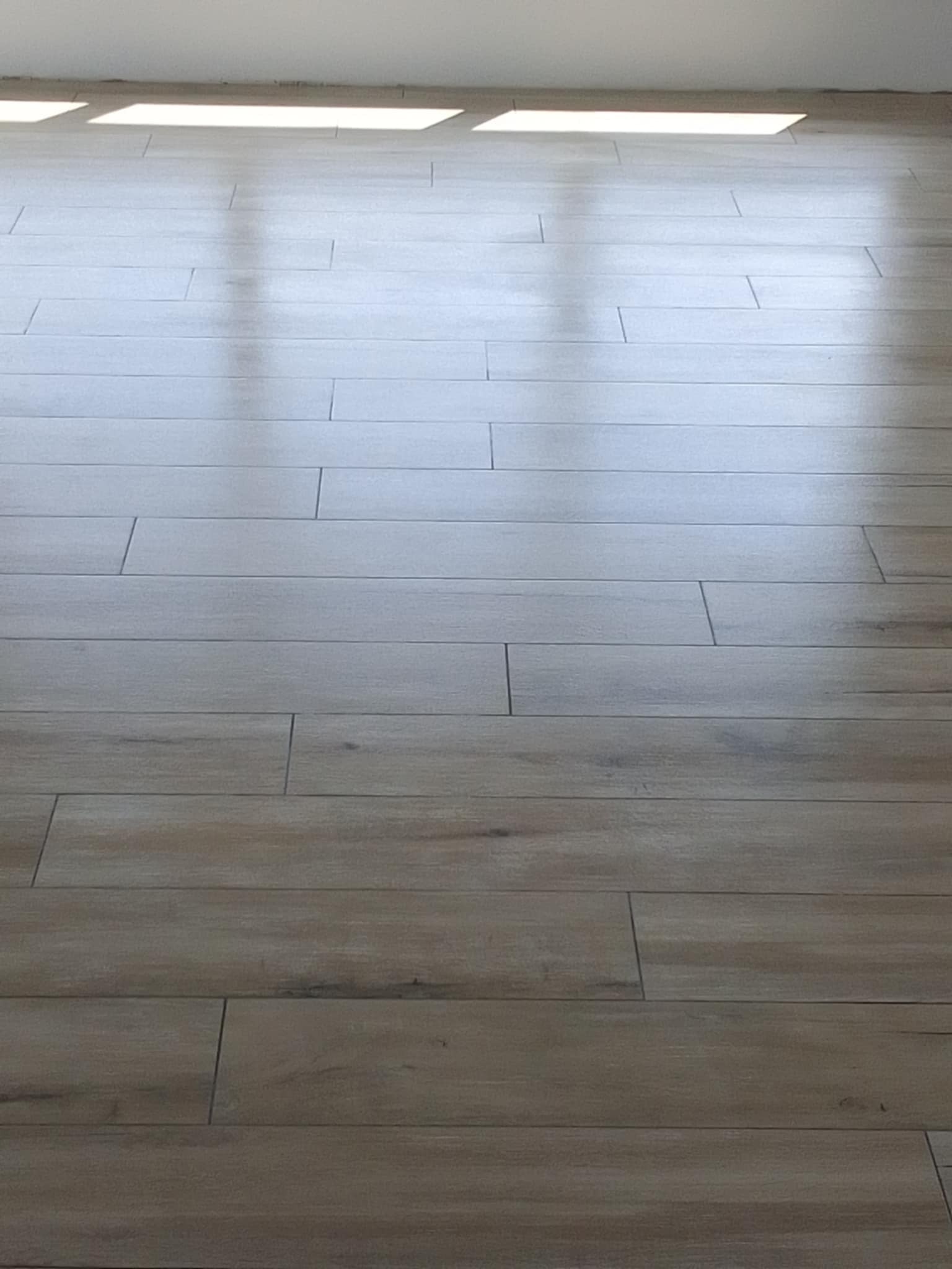 Ułożona podłoga z paneli imitujących drewno w jasnym odcieniu, widoczne fugi i odbicie światła słonecznego na powierzchni.