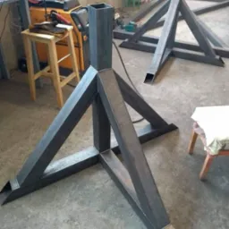 Metalowe, spawane konstrukcje wsporcze w kształcie trójkątów, z profili zamkniętych, widoczne narzędzia i sprzęt spawalniczy w tle.