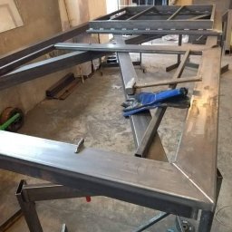 Usługi spawalnicze Spawanie TIG Spawacz MIG MAG MobiusMetal - Konstrukcja stalowa w trakcie budowy, widoczne ramy i profile, narzędzia pracy: młotek i rękawice robocze leżą na elemencie konstrukcji.