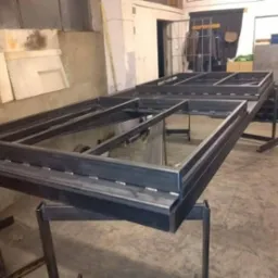 Surowa, metalowa rama bramy wjazdowej z profili, w trakcie spawania na stole warsztatowym, widoczne ślady spawania i niedoskonałości wykończenia, w tle warsztat.