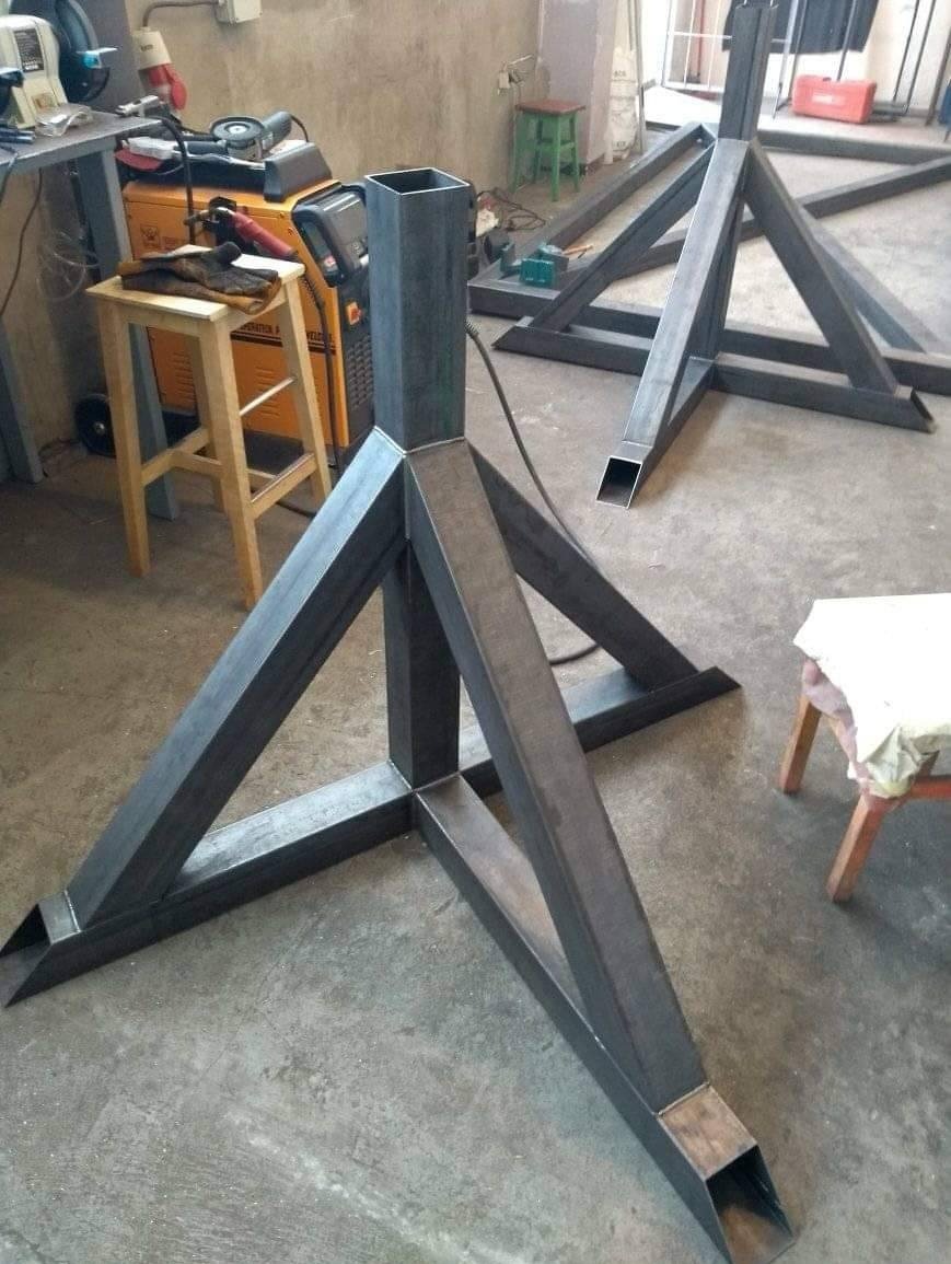 Metalowe, spawane konstrukcje wsporcze w kształcie trójkątów, z profili zamkniętych, widoczne narzędzia i sprzęt spawalniczy w tle.