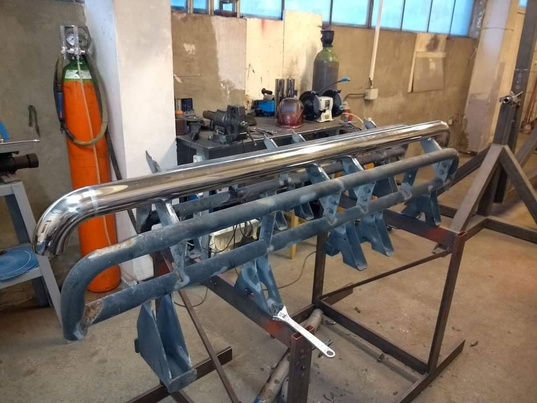 Element konstrukcji metalowej, prawdopodobnie fragment ramy lub zabezpieczenia, składający się z rur i wsporników, umieszczony na metalowym stojaku w warsztacie, widoczny klucz francuski i butle...