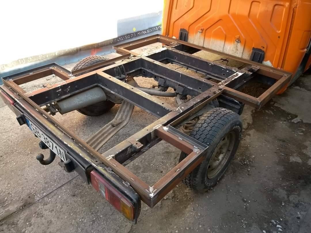 Rama metalowa, prawdopodobnie przyczepki samochodowej, w trakcie spawania, widoczne spawy na profilach, fragment pomarańczowej karoserii pojazdu w tle.