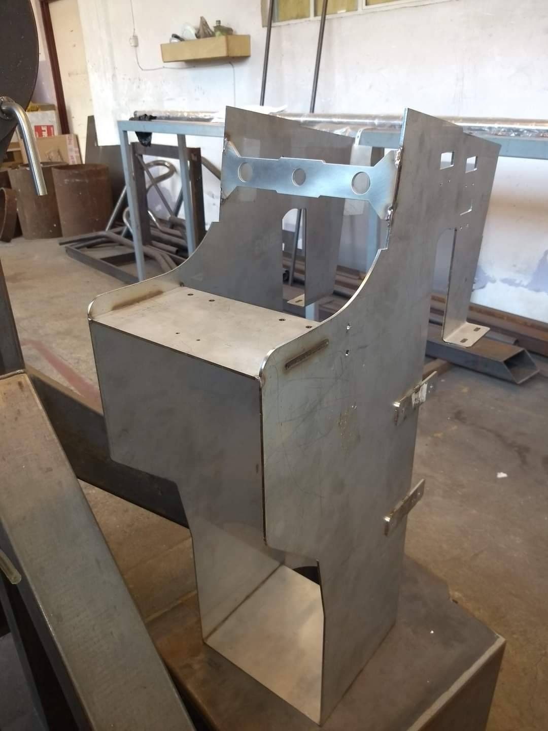 Metalowa konstrukcja spawana w kształcie obudowy automatu do gier, widoczne ślady spawania i surowy wygląd metalu, w tle warsztat.