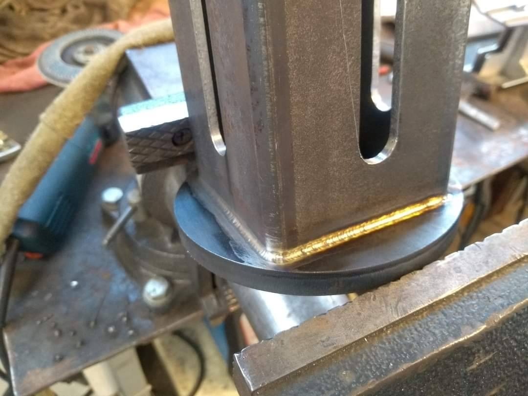 Detal spawu narożnego na profilu stalowym z wyciętymi otworami, zamocowanym w imadle; widoczne ślady obróbki i narzędzia w tle.