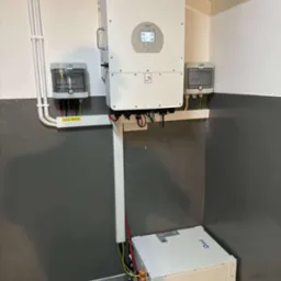 Kompletna instalacja magazynu energii Deye w pomieszczeniu: dwa akumulatory, inwerter z ekranem i zabezpieczenia. Szare ściany, kable w listwach.