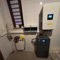 GLOBCORE Sp. z o.o. - Instalacja magazynu energii w pomieszczeniu z wykończeniem w płytkach, Żyrardów. Widoczny inwerter, akumulator i zabezpieczenia. Elementy instalacji elektrycznej.