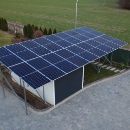 GLOBCORE Sp. z o.o. - Zadaszenie z paneli słonecznych nad garażem, widok z góry. Na podwórku kostka brukowa, trawnik i żółty samochód dostawczy w tle. Nowoczesna instalacja.