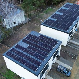 GLOBCORE Sp. z o.o. - Widok z góry na dwa nowoczesne budynki z panelami słonecznymi na dachach, zaparkowane samochody i otaczającą zieleń. Jeden budynek w trakcie budowy w tle.