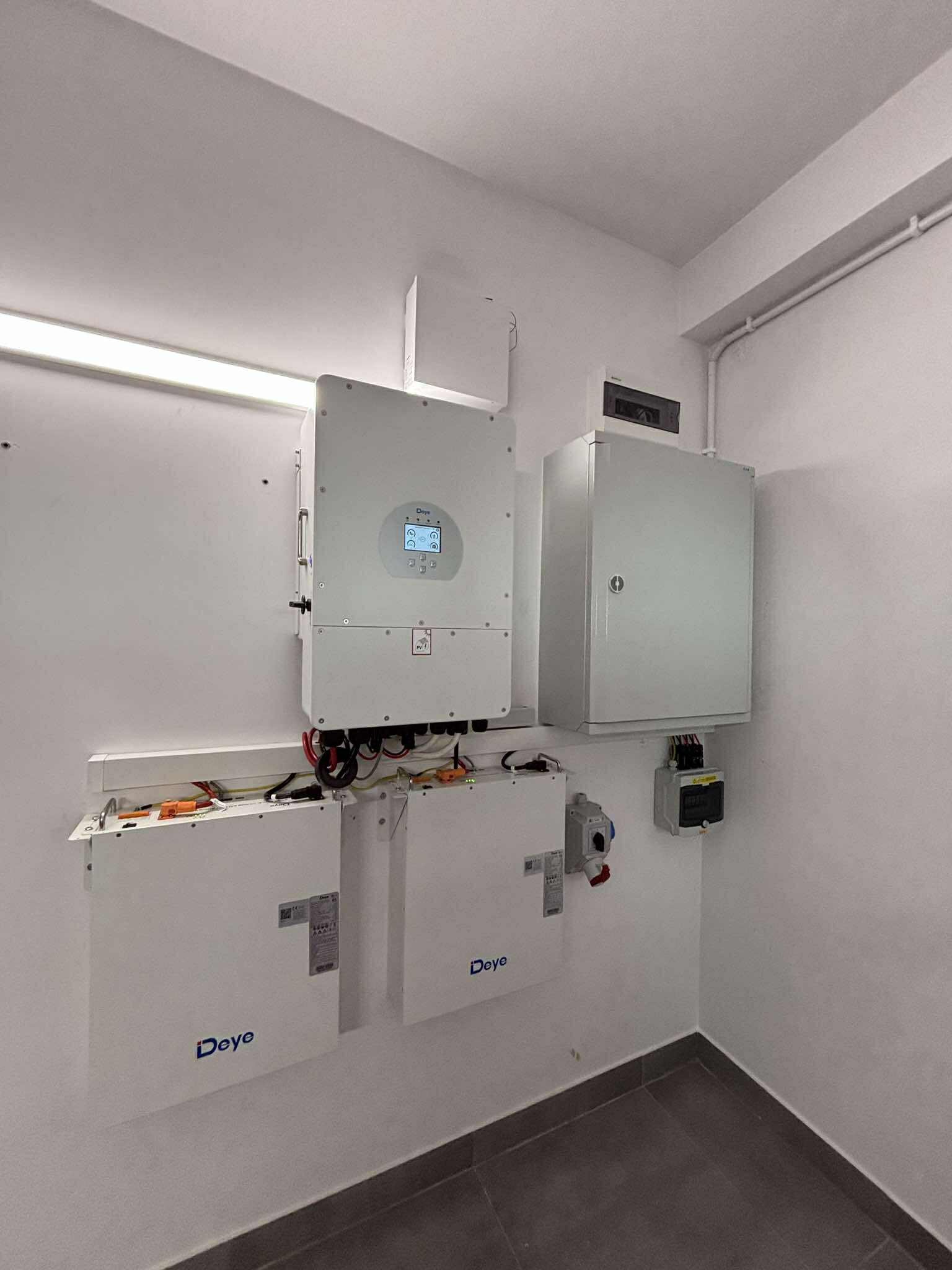 Białe magazyny energii Deye i inwerter fotowoltaiczny zamontowane na ścianie w pomieszczeniu. Widoczne kable i instalacja elektryczna.