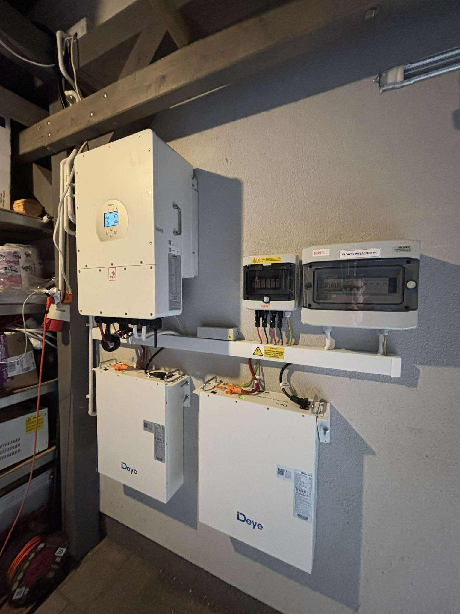 Kompletna instalacja magazynu energii Deye zamontowana na ścianie w pomieszczeniu, widoczne skrzynki rozdzielcze i okablowanie.
