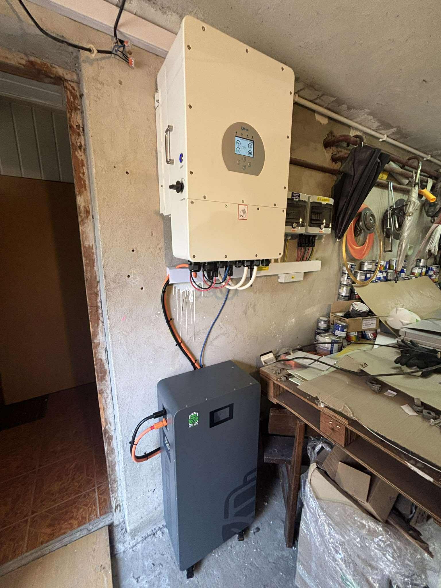 Zamontowany inwerter fotowoltaiczny z podłączonym magazynem energii w pomieszczeniu gospodarczym. Widoczne przewody, skrzynka elektryczna i wyposażenie warsztatowe.