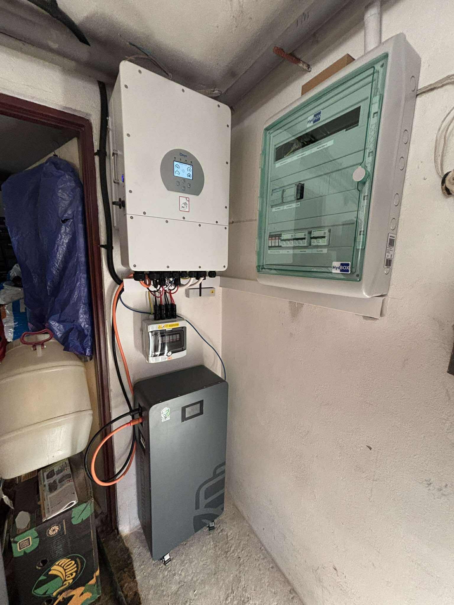 Montaż domowej instalacji fotowoltaicznej: inwerter, rozdzielnica i akumulator na ścianie. Widoczne okablowanie i elementy zabezpieczeń.