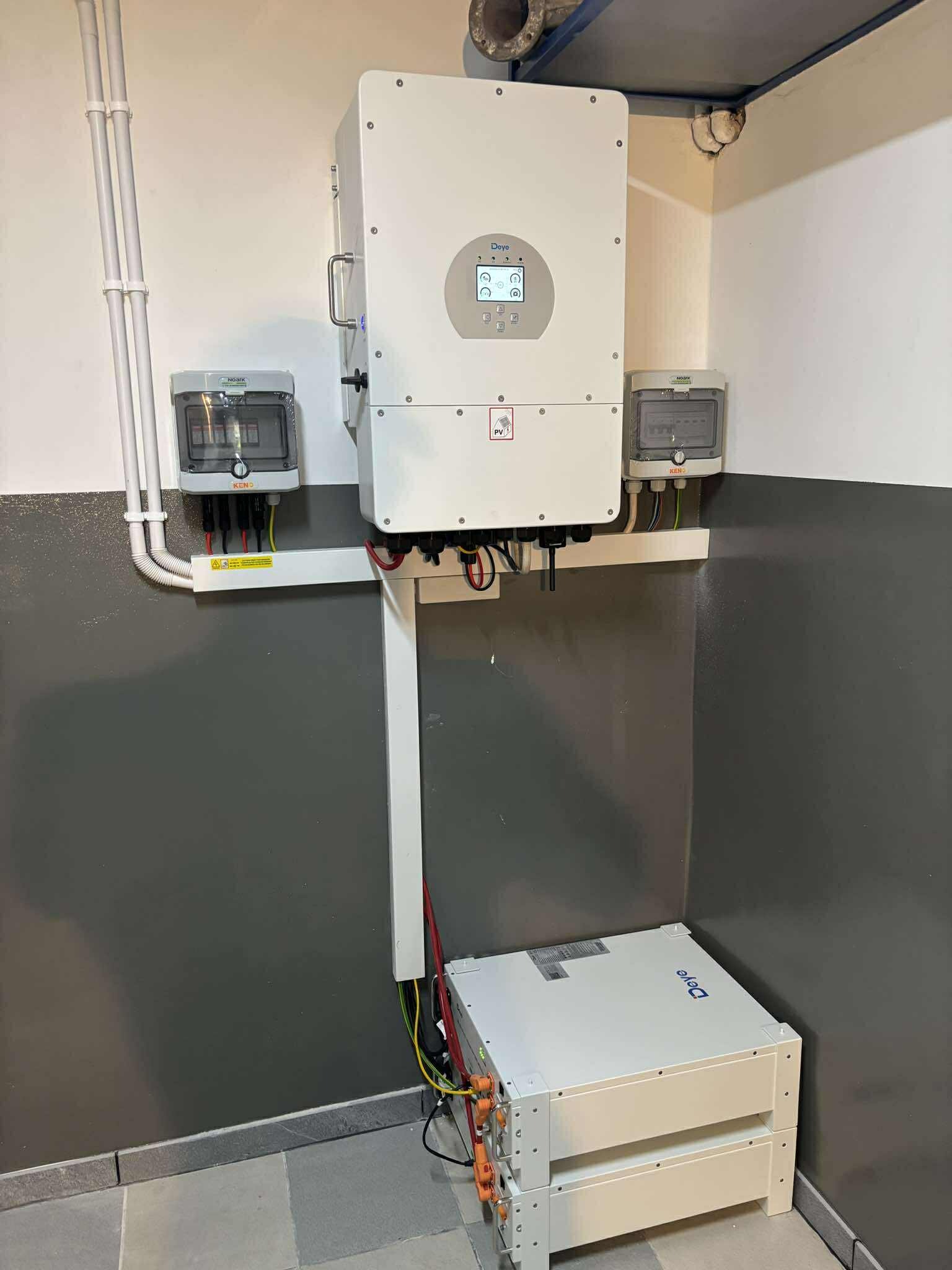 Kompletna instalacja magazynu energii Deye w pomieszczeniu: dwa akumulatory, inwerter z ekranem i zabezpieczenia. Szare ściany, kable w listwach.