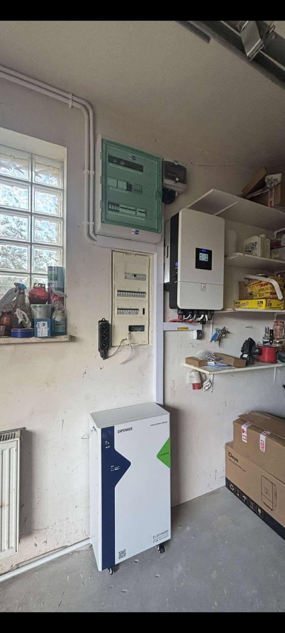 Instalacja magazynu energii DiPower i falownika w garażu w Żyrardowie. Widoczne skrzynki elektryczne na ścianie i półki z narzędziami.