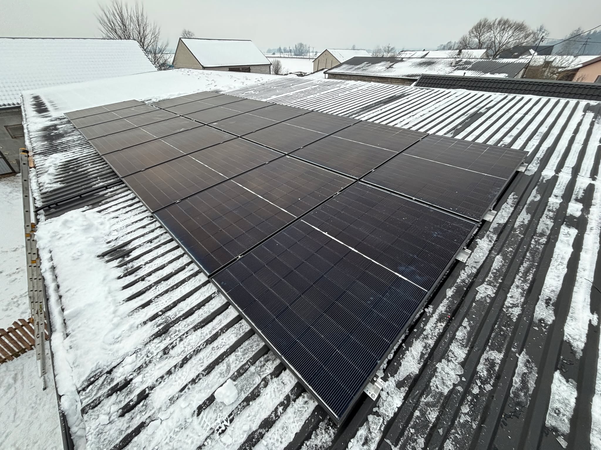 Panele słoneczne na dachu pokrytym śniegiem, widok z góry. Instalacja fotowoltaiczna w zimowej scenerii. Metalowa konstrukcja dachu.