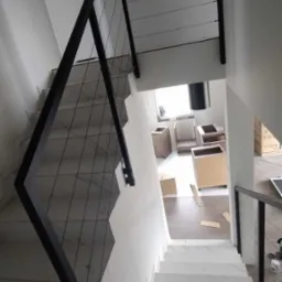 Wewnętrzne schody wykończone białym marmurem z czarną, minimalistyczną balustradą z cienkich, poziomych linek, widziane z góry w trakcie montażu zabudowy kuchennej.