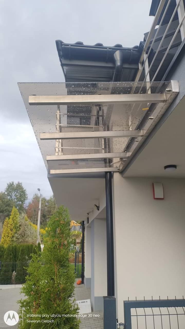 Zadaszenie wejściowe z przezroczystego tworzywa i metalowych wsporników, widoczne krople deszczu, nowoczesny design.