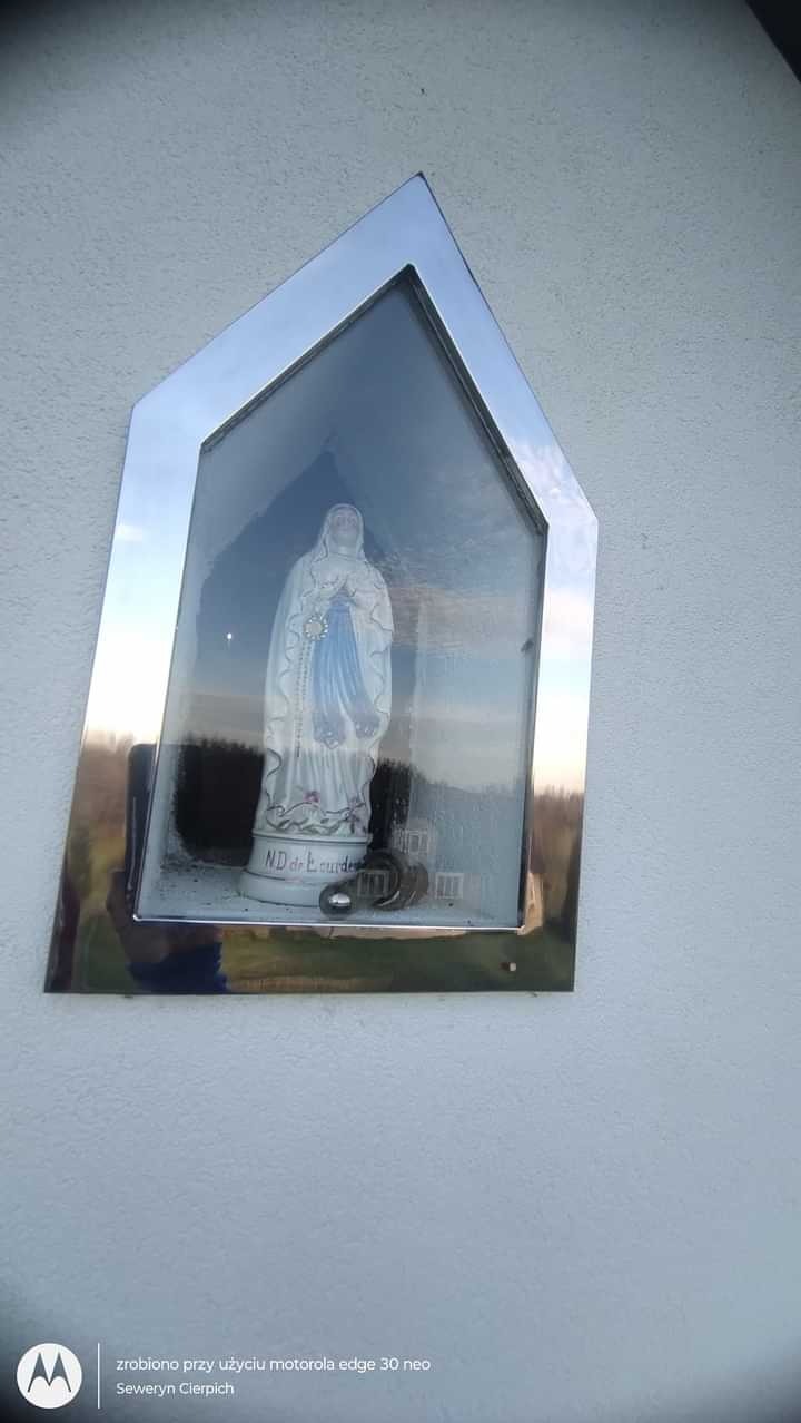 Nisza z figurką Matki Boskiej w metalowej, srebrnej obudowie zamontowana na zewnętrznej ścianie budynku.