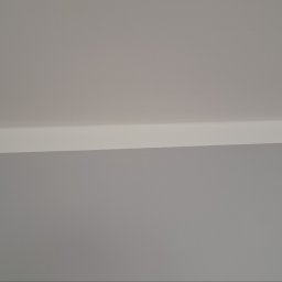 Volodymyr Svirko - Pomieszczenie po malowaniu: gładka, szara ściana spotyka się z białym sufitem pod kątem prostym, widoczny fragment listwy przysufitowej.
