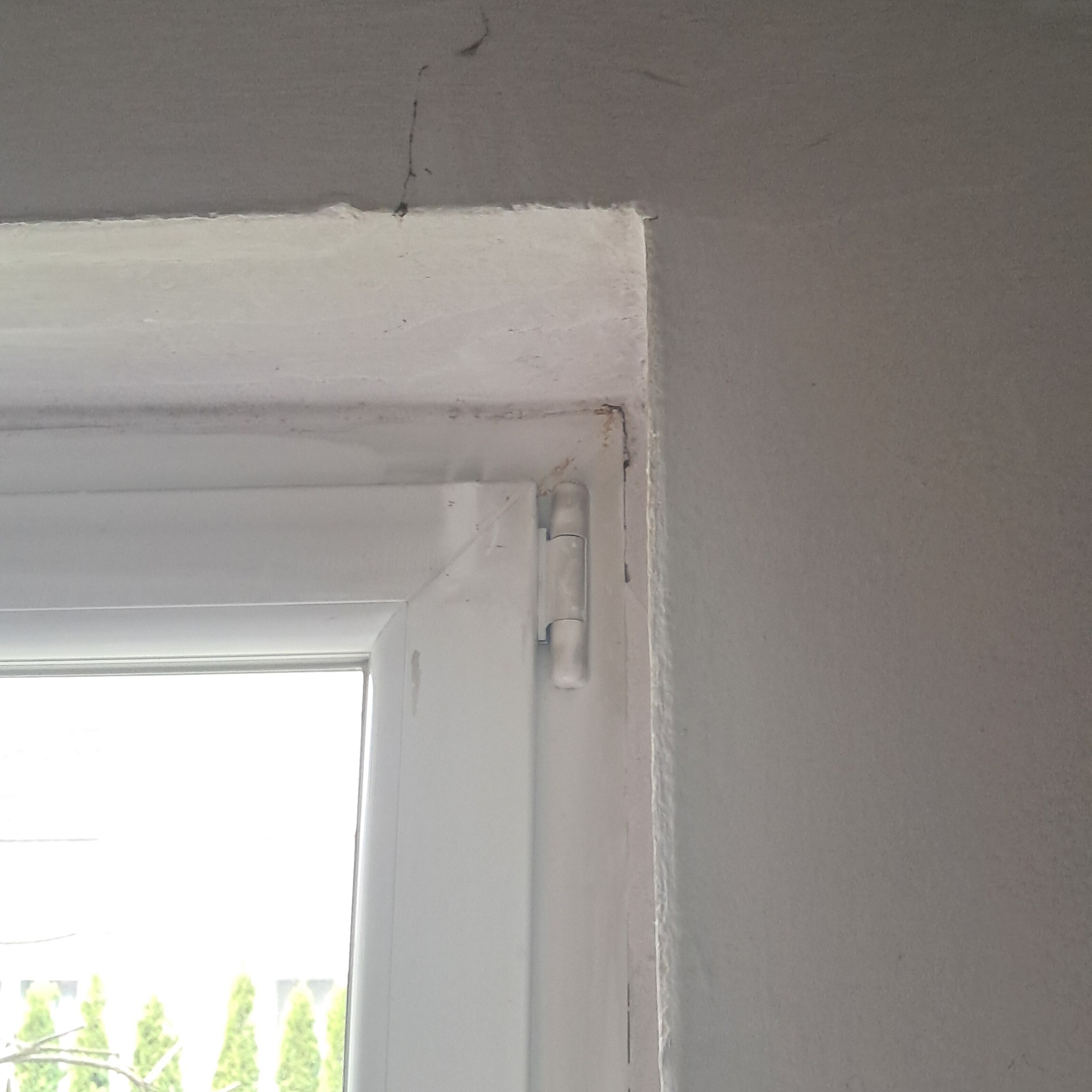 Fragment ściany po obróbce, widoczne łączenie z ościeżnicą okienną, nierówności i ślady po szpachlowaniu oraz malowaniu.