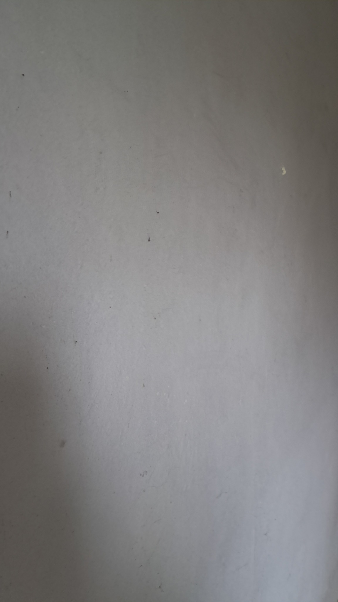 Szara, gładka ściana z drobnymi niedoskonałościami i zróżnicowanym oświetleniem.