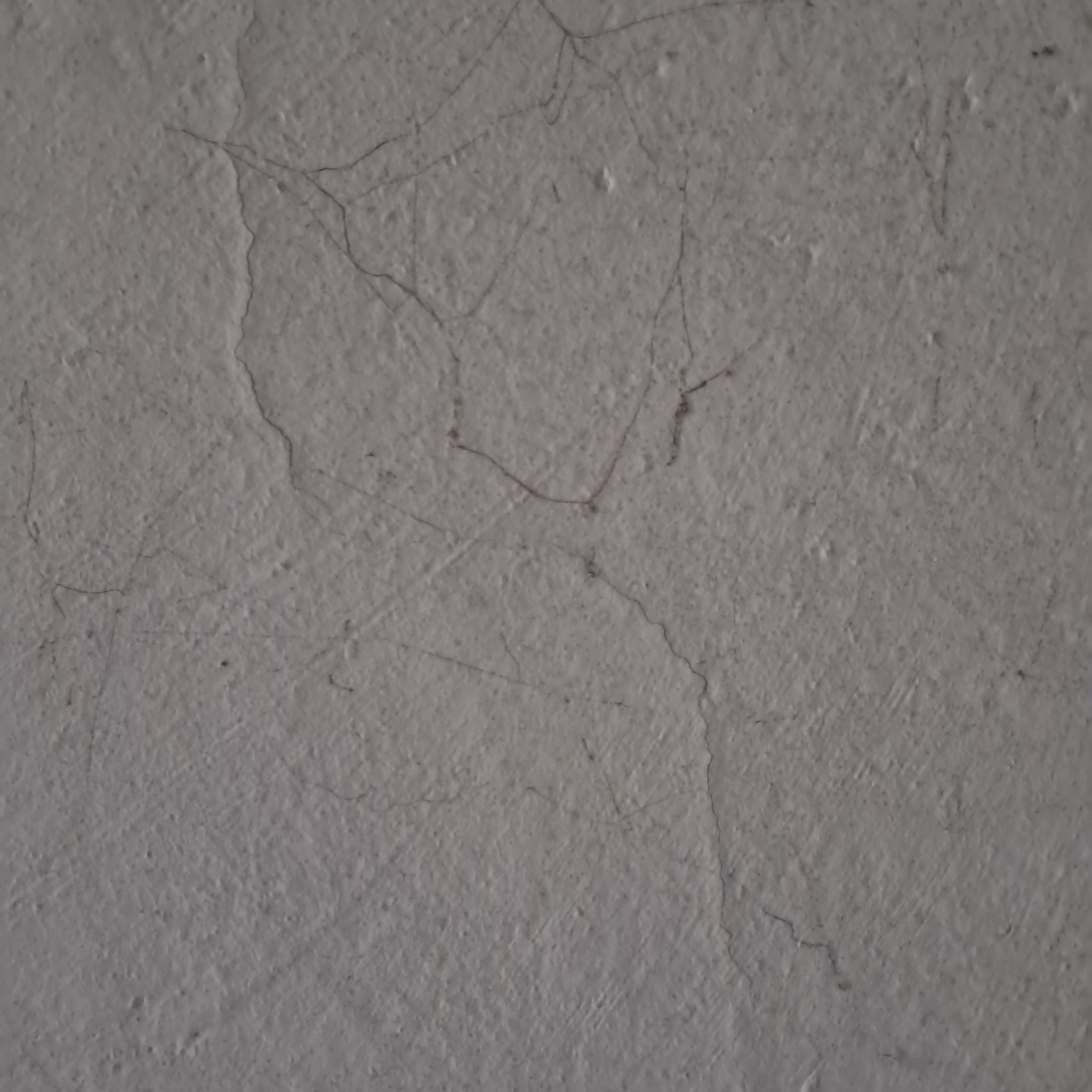 Szara ściana z widocznymi drobnymi rysami i nierównościami na powierzchni.