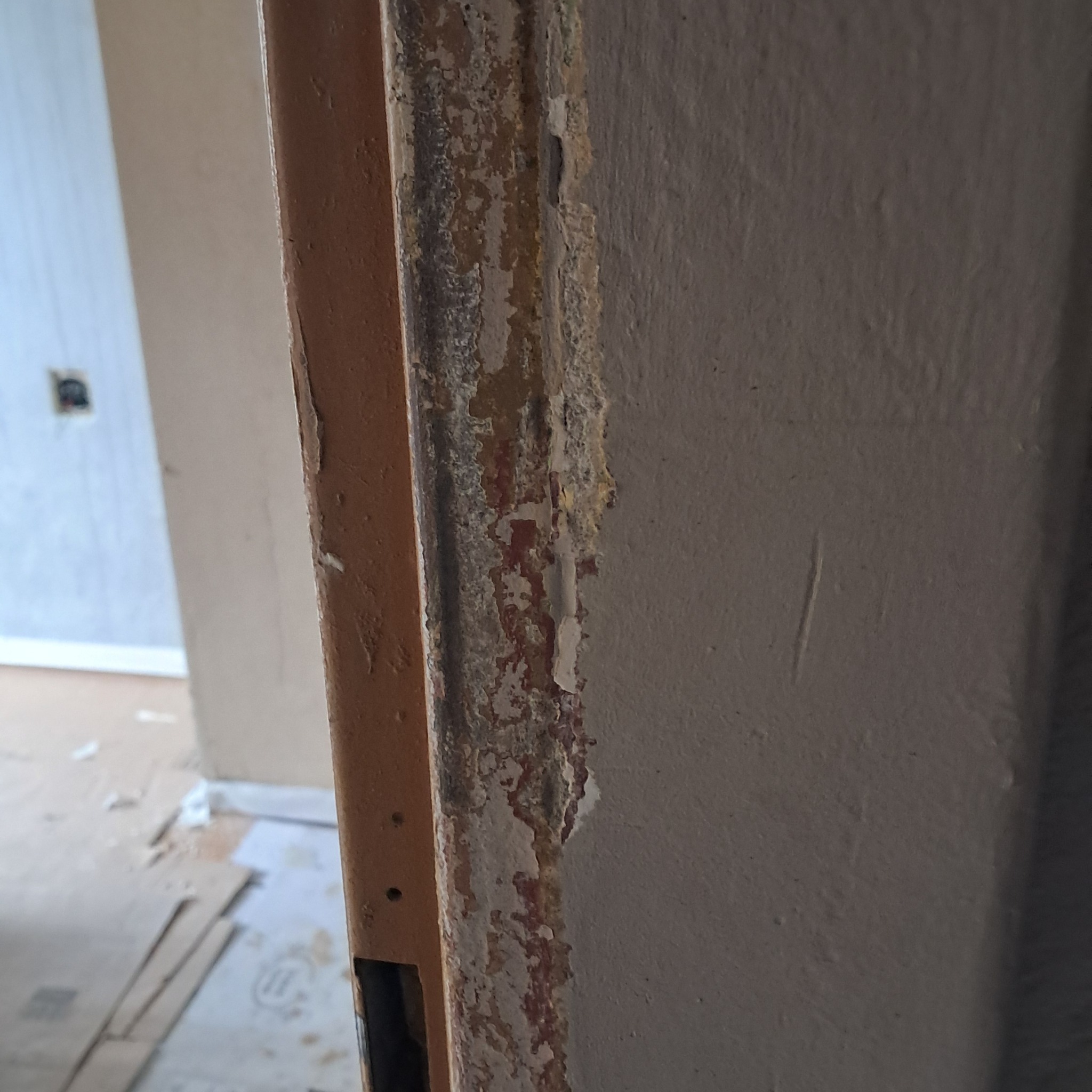 Ościeżnica z widocznymi śladami starej farby i przygotowaniem do ponownego malowania, obok fragment ściany z nierówną powierzchnią.