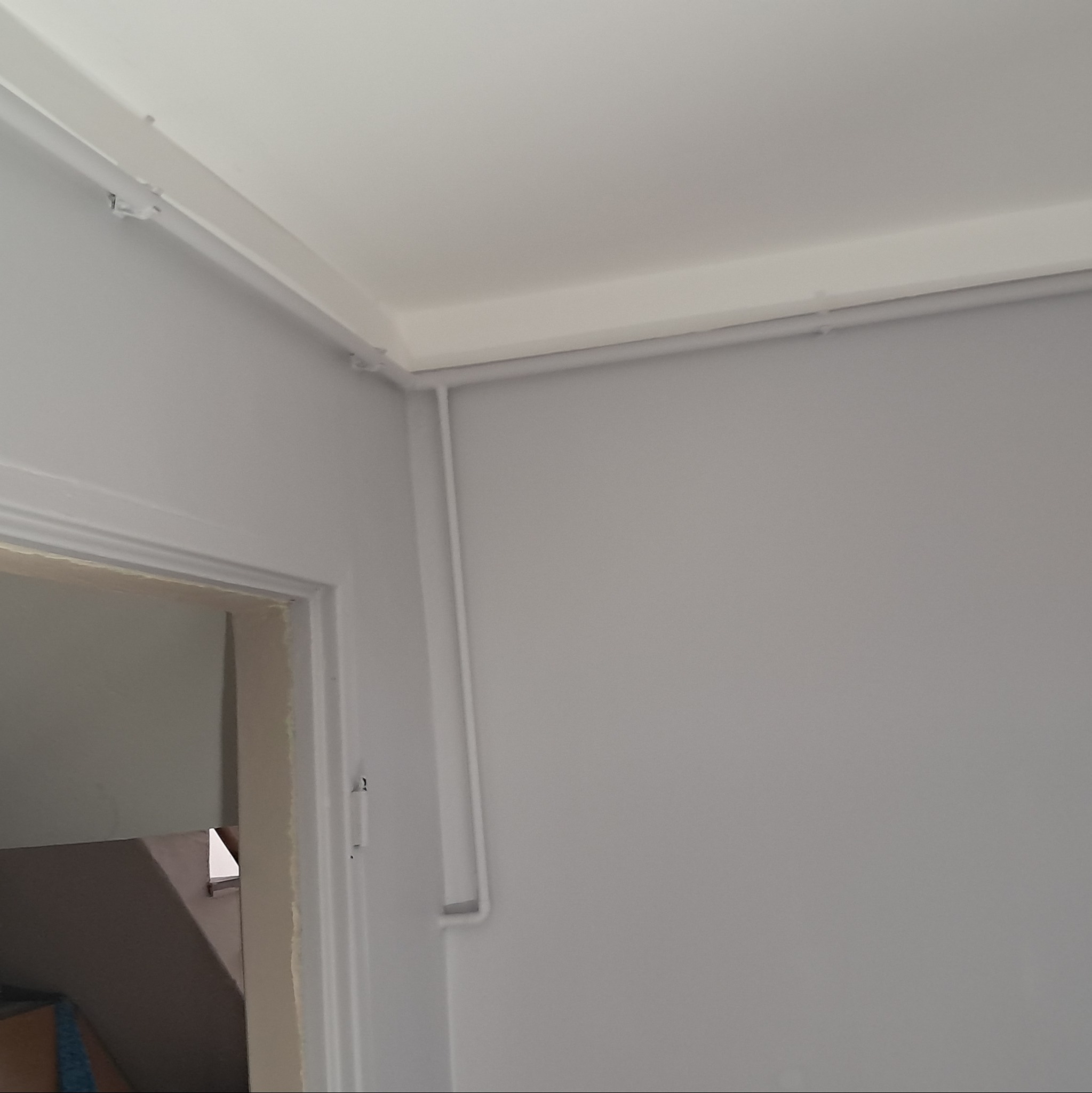 Szare ściany i biały sufit po remoncie, widoczne listwy przypodłogowe i fragment futryny drzwiowej prowadzącej na schody.