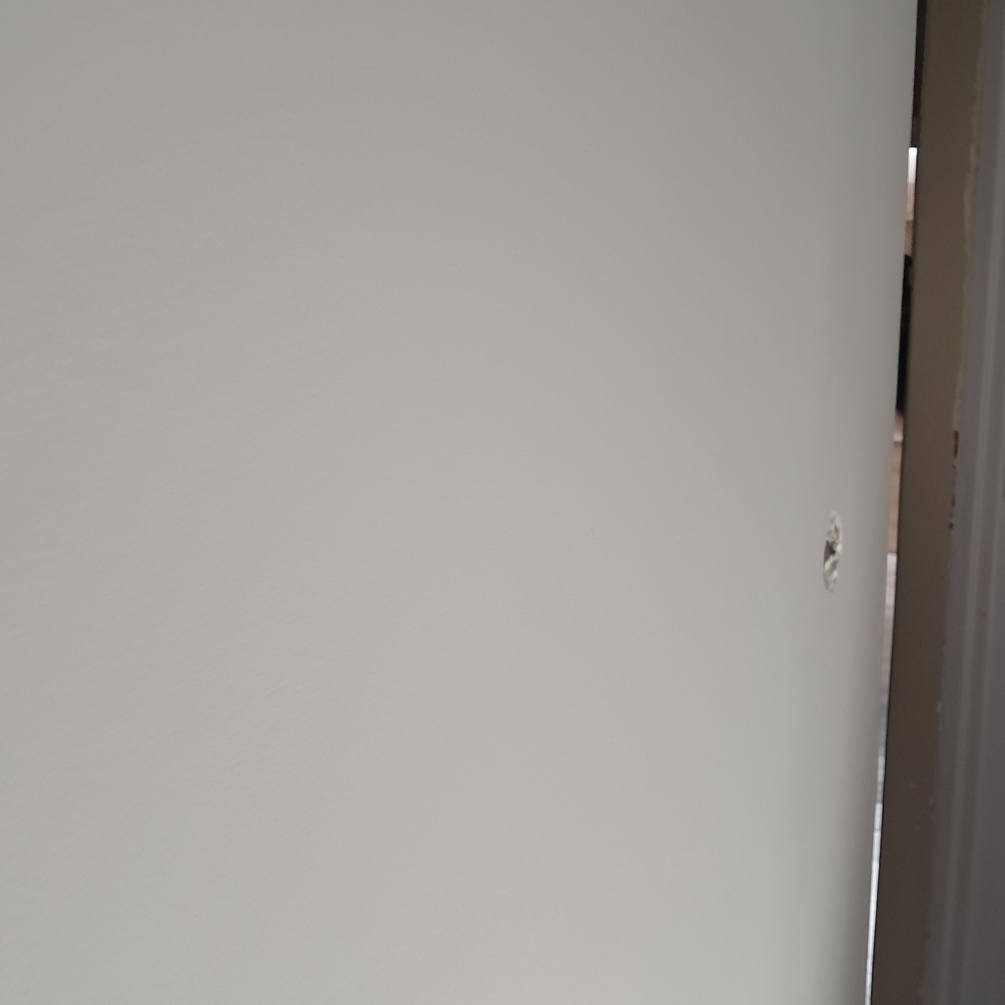 Świeżo pomalowana, jasna ściana z widocznym otworem po kołku. Ujęcie z bliska, ukazujące strukturę farby i niedoskonałość powierzchni.