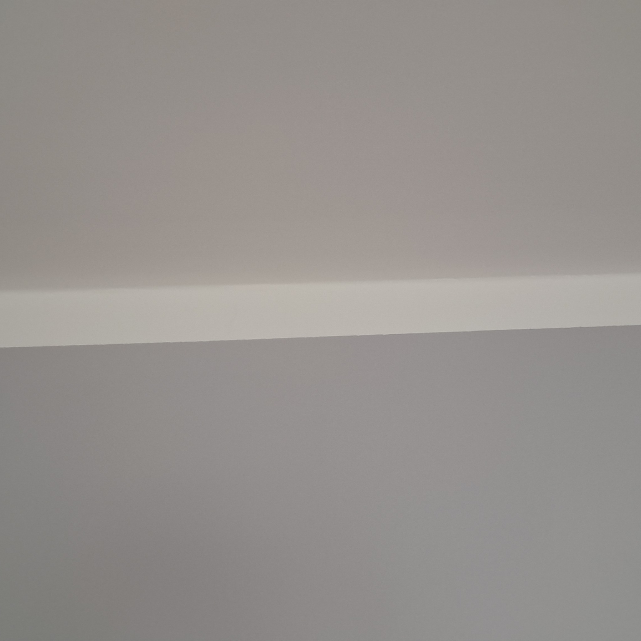 Pomieszczenie po malowaniu: gładka, szara ściana spotyka się z białym sufitem pod kątem prostym, widoczny fragment listwy przysufitowej.