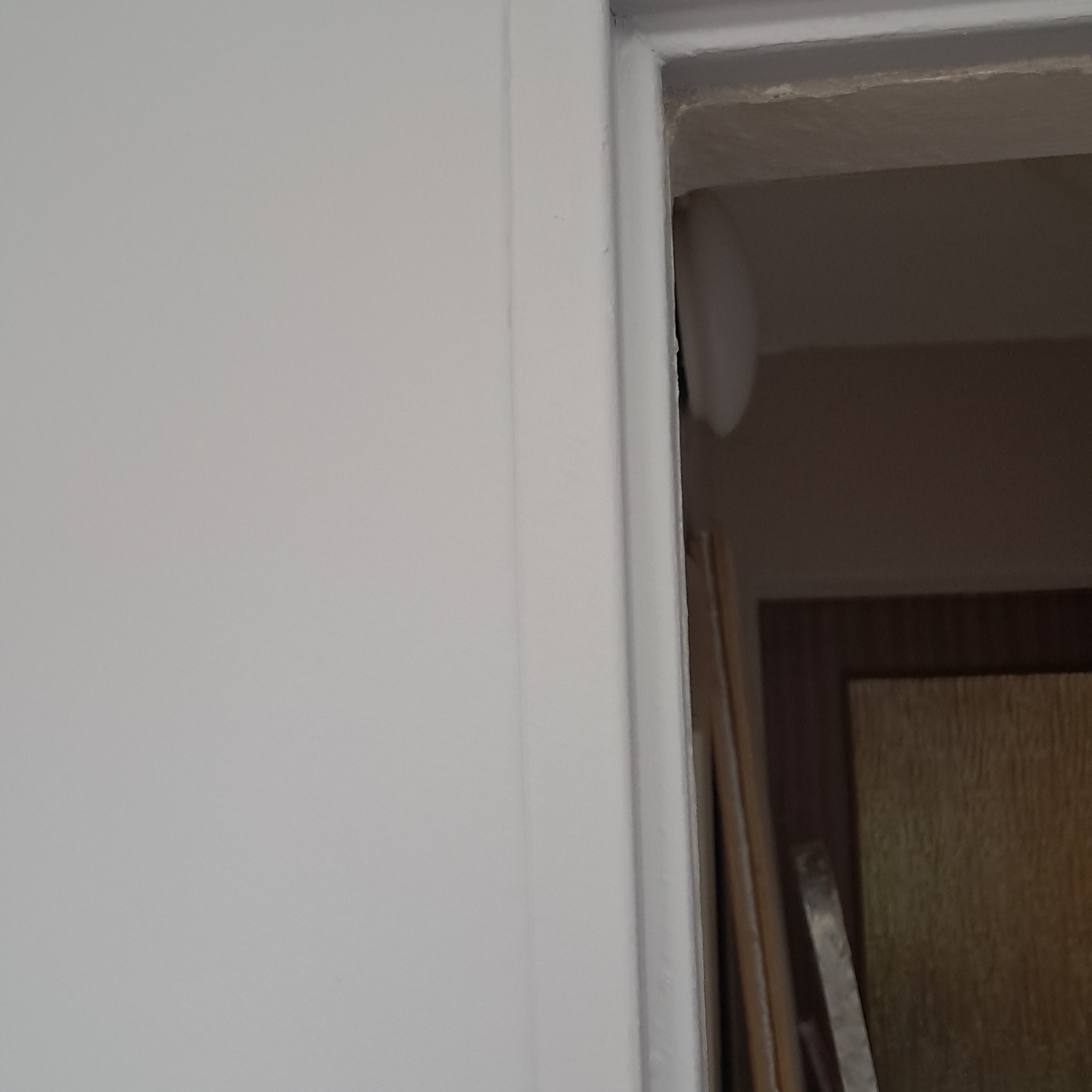 Świeżo pomalowana na biało framuga drzwi z widocznymi narzędziami w tle, po prawej stronie u góry widać niedomalowany fragment sufitu.