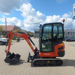 CHOGI SPÓŁKA Z OGRANICZONĄ ODPOWIEDZIALNOŚCIĄ - Pomarańczowa mini koparka Kubota KX018-4 z trzema łyżkami na kostce brukowej, na tle budynku z logo firmy CHOGI.