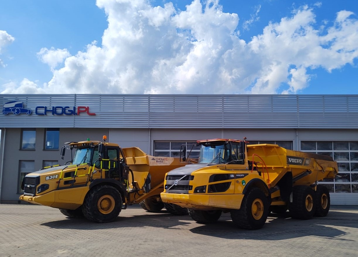 Dwa żółte wozidła przegubowe Volvo B30E i A35G na tle budynku z logo CHOGI.PL i błękitnego nieba z chmurami.
